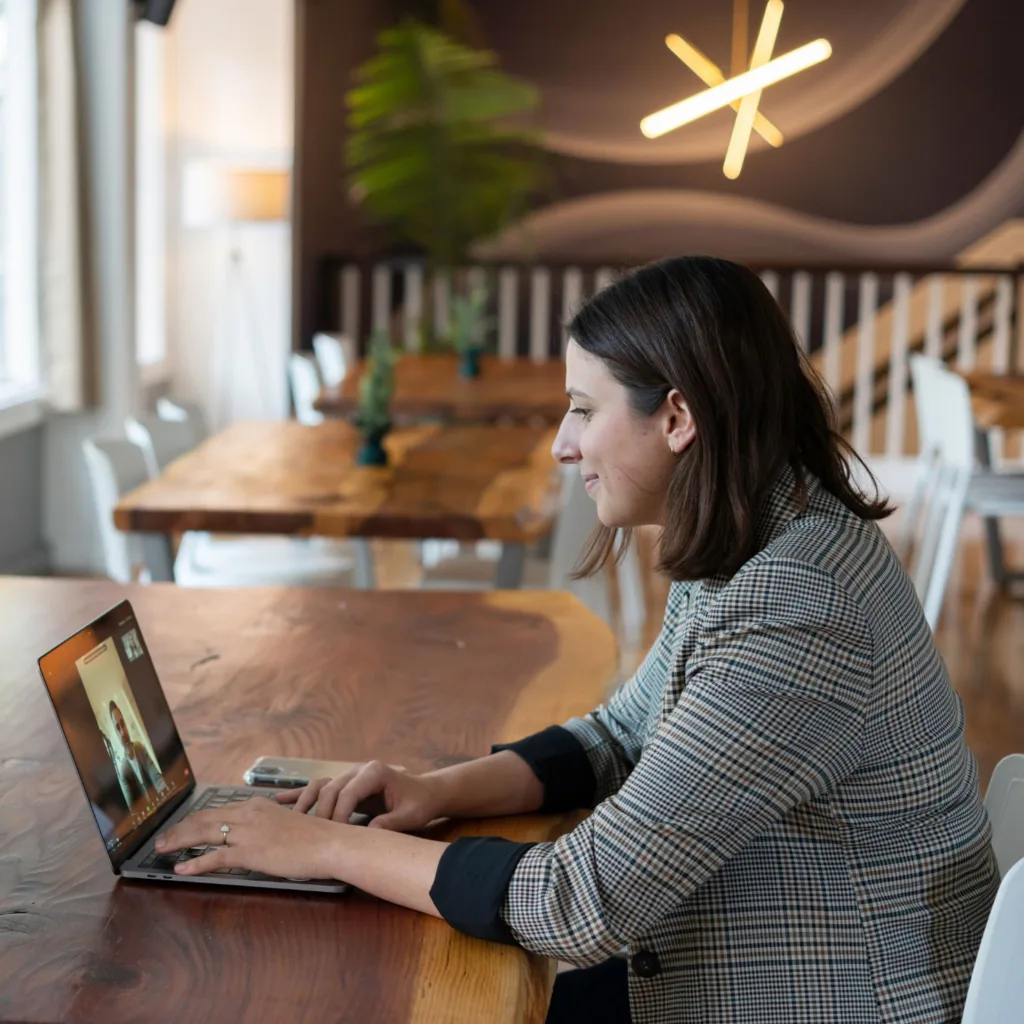 A woman seated at a table, talking to someone on a videoconference call.